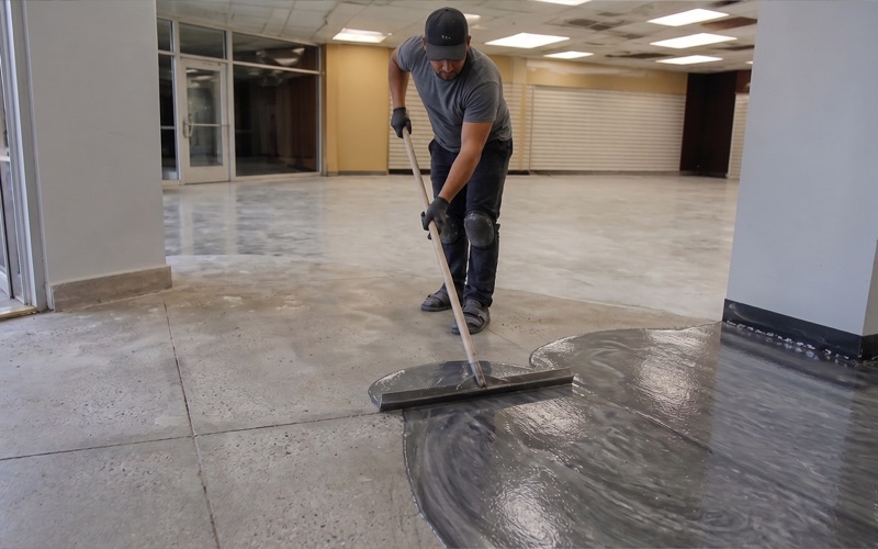 Worker drawing a squeegee through a wet metallic pour, pigment visibly moving in the film