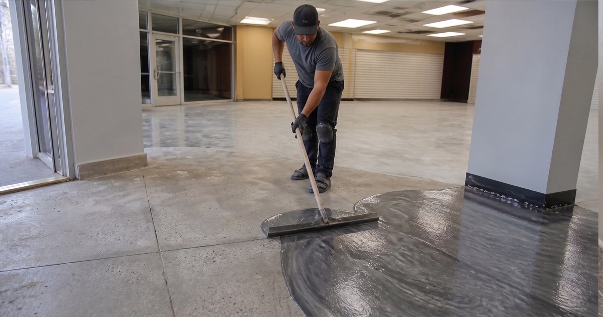 Worker drawing a squeegee through a wet metallic pour, pigment visibly moving in the film